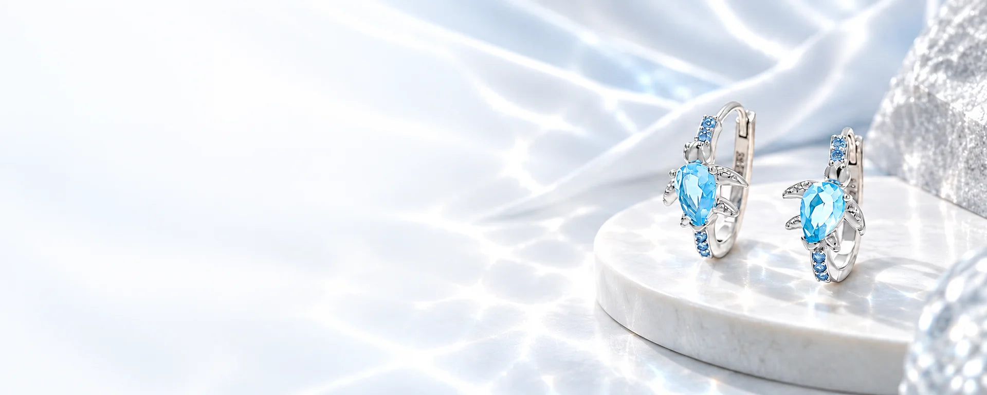 Silver hoops with pale blue stones, resting in soft silver light
